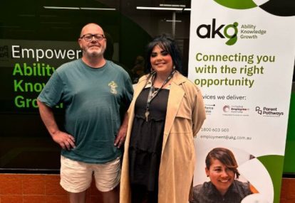 Adam (L) and Shana (R) stand smiling and proud in front of an AKG banner.