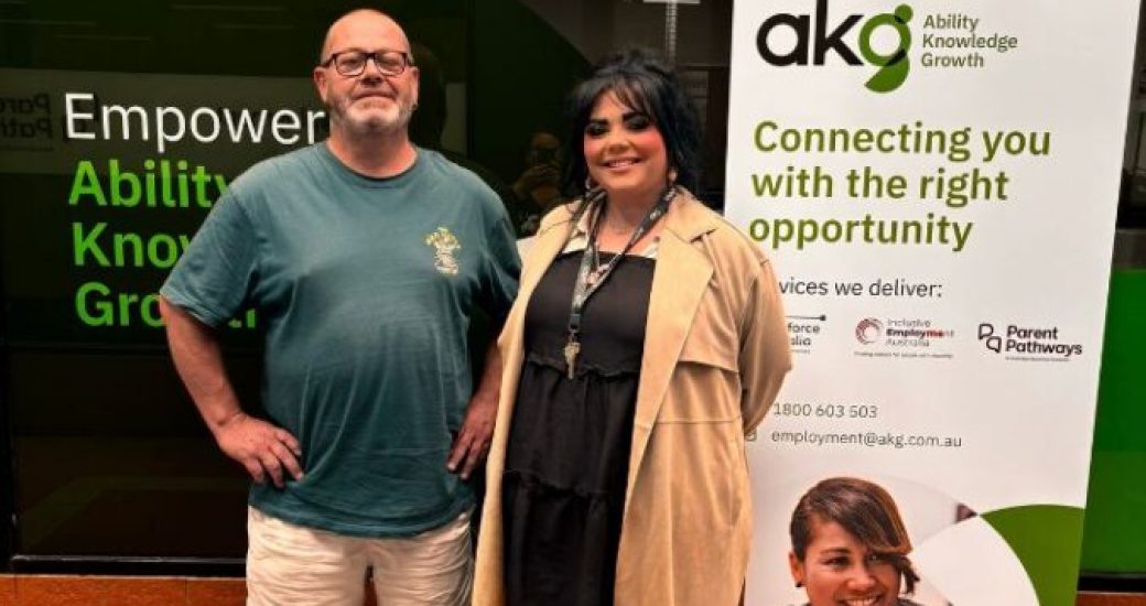 Adam (L) and Shana (R) stand smiling and proud in front of an AKG banner.